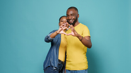 Affectionate couple doing heart shape symbol with hands in studio. Man and woman advertising...