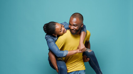 Playful couple having fun with piggy back ride in front of camera. Man carrying woman and enjoying...