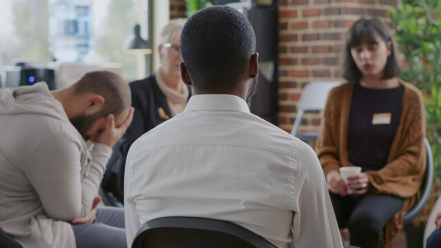 Close up of african american man discussing alcohol addiction at aa therapy session. Adult making confession in front of support group people at rehabilitation program meeting.