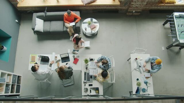 Top view of employees diverse group working in shared office talking sitting at desks cooperating. Modern business locations and young workers concept.