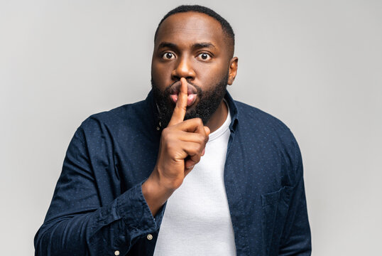 Keep the silence. African-American guy holding index finger near lips in shh gesture, calls to be quieter, keep a private secret, hush and do not talking