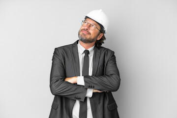 Young architect man with helmet over isolated background looking up while smiling
