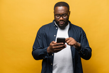 Photo of attractive bearded black man in casual shirt using smartphone isolated over grey background, touches phone screen, necessary tool for productivity, finds inspiration online