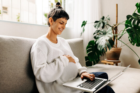 Happy pregnant woman video calling her friends at home - Powered by Adobe