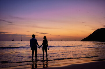 Romance on the sea shore. Silhouette of a couple in love holding hands on a sunset tropical background.