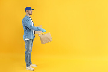 Delivery man holds bag with food and box on yellow background