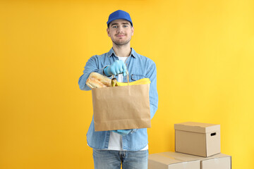 Delivery man holds bag with food on yellow background