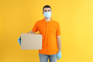 Delivery man in gloves and mask holds box on yellow background