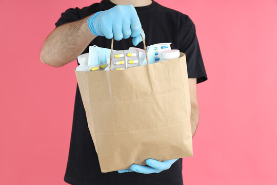 Delivery man holds bag with medicines on pink background