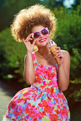 Portrait of fashion girl in pink dress and hairstyle in park eating tce-cream.