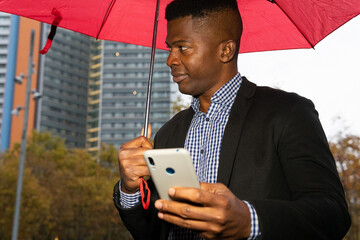 African american man with a red umbrella using the mobile. Rain concept