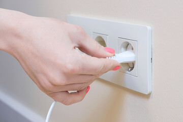 Naklejka premium The woman pulls the electrical plug out of the socket wire