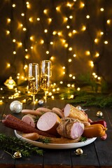 Fresh sausages and hams on new year or Christmas celebration table with champagne glasses and bokeh lights, delicious snack, spicy and high quality meat products made of pork and veal, beef.