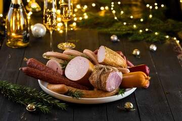 Fresh sausages and hams on new year or Christmas celebration table with champagne glasses and bokeh...