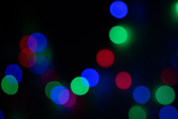 Defocused bokeh lights on black background, an abstract naturally blurred backdrop for Christmas eve or birthday party. Festive light texture. Colorful garland in blur. Overlay effect for design