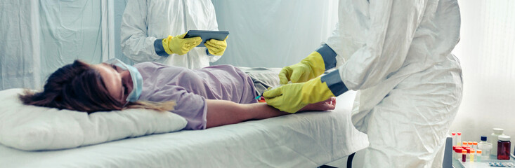 Obraz premium Doctors in bacteriological protection suit taking blood sample from patient lying on a gurney in a field hospital