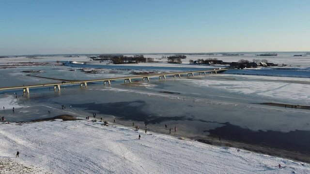 Ice skating people on a frozen Reevediep lake during a beautiful winter day in Overijssel, The Netherlands. Aerial drone point of view.