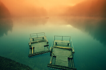 Two old wooden rafts on the lake on a foggy morning. Synevyr, Ukraine