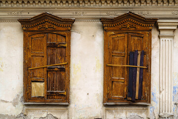 Carved windows with closed wooden shutters on the facade of a dilapidated old building. The picture was taken in Russia, in the city of Orenburg - obrazy, fototapety, plakaty