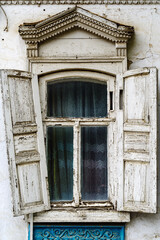 Fototapeta na wymiar A window with wooden shutters and carved frames of the old house, with stucco elements on the facade. The picture was taken in Russia, in the city of Orenburg