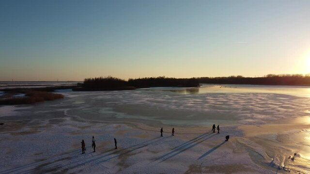 Ice skating people on a frozen lake during a beautiful winter sunset at the Drontermeer in The Netherlands. Aerial drone point of view.