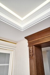 Decorated wooden doorway with carved furniture brackets and fluted panel in light spacious room with contemporary led backlight on ceiling © timltv