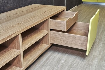 Elegant TV stand made of oak wood veneer with bright yellow facade and open drawers in minimal style near dark cork wall in living room