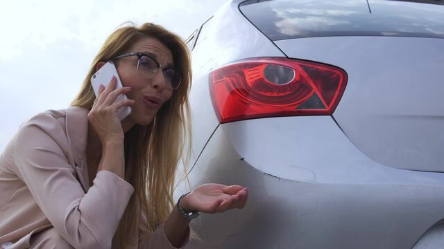Confused blond woman finding scratch on rear bumper of her car calling to police