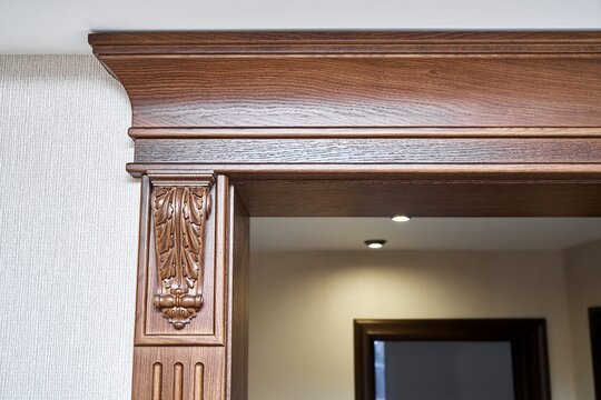 Decorated wooden doorway with carved furniture brackets and crown molding in classic style in light spacious room closeup