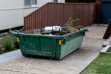 Skip bin with household waste rubbish on a front yard. House clean up concept. - obrazy, fototapety, plakaty