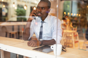 Businessman drinking coffee in cafe. Handsome African man talking to the phone while enjoying in fresh coffee..