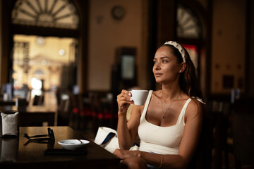 Stylish young woman drinking coffee at cafe. Beautiful girl enjoy in fresh coffee.