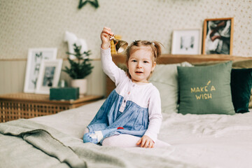 Naklejka premium A happy girl is playing on the bed on Christmas morning in a room decorated for Christmas or New Year. Childhood, festive morning, Christmas mood
