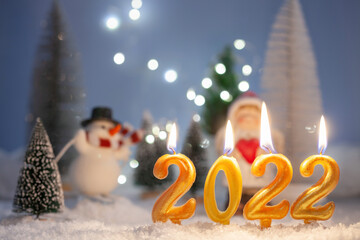 Candles with numbers 2022 and  Christmas forest background with trees and figures. New Year concept