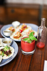 A red fruity drink with mint, tacos on the background, wooden table in a restaurant 