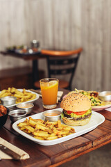 A plate with a burger, French fries, orange lemonade on a wooden table in a restaurant 
