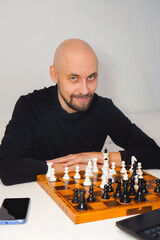 Bald man wearing beard playing chess on board near laptop. Strategy and competition concept.