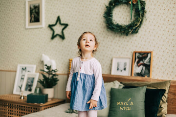A happy girl is playing on the bed on Christmas morning in a room decorated for Christmas or New Year. Childhood, festive morning, Christmas mood