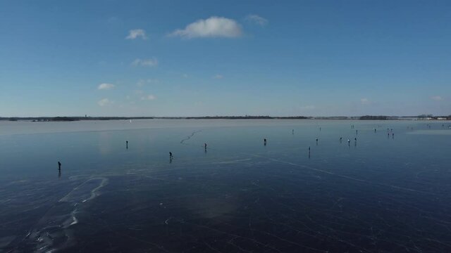 Ice skating people on a frozen lake in the Wieden Weerribben nature reserve during a beautiful winter day in The Netherlands. Aerial drone point of view.