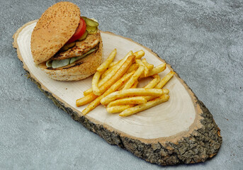 Close-up of tasty chicken burger with french fries tomato and cucumber pickle on a natural wooden tray