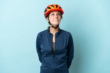 Young cyclist woman isolated on blue background and looking up - obrazy, fototapety, plakaty