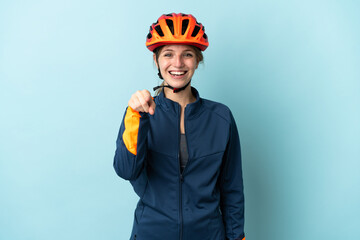 Young cyclist woman isolated on blue background surprised and pointing front - obrazy, fototapety, plakaty