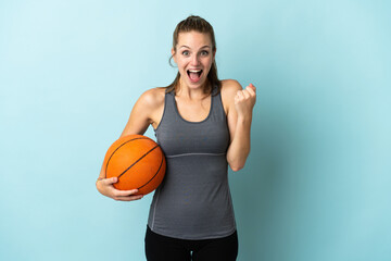 Young woman playing basketball isolated on blue background celebrating a victory in winner position