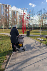Obraz premium Mom with a baby carriage in an autumn day in a city park on a cobbled stone tiled walkway