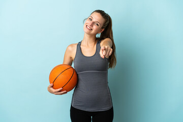 Young woman playing basketball isolated on blue background pointing front with happy expression