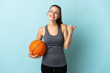 Young woman playing basketball isolated on blue background pointing to the side to present a product