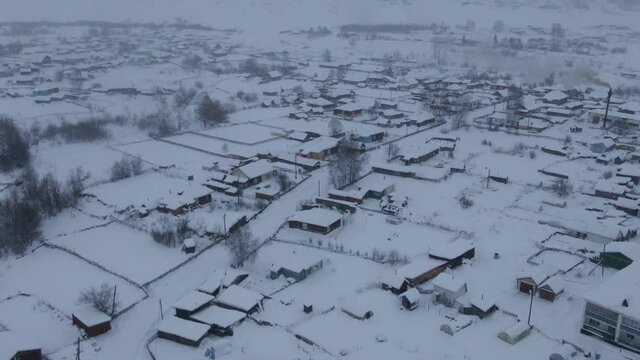 Aerial shot in landing movement over snowed town when strong snow-storm in evening