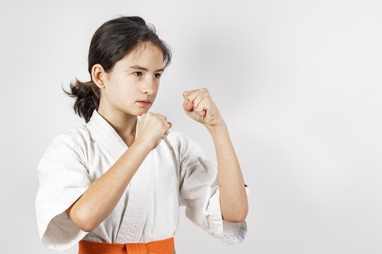Karate girl on a white background. Sporty caucasian brunette in a white kimono with an orange belt. Contact sports. Oriental martial arts. Healthy lifestyle and self defense concept. Copy space