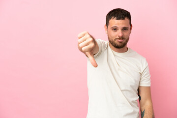 Young Brazilian man isolated on pink background showing thumb down with negative expression