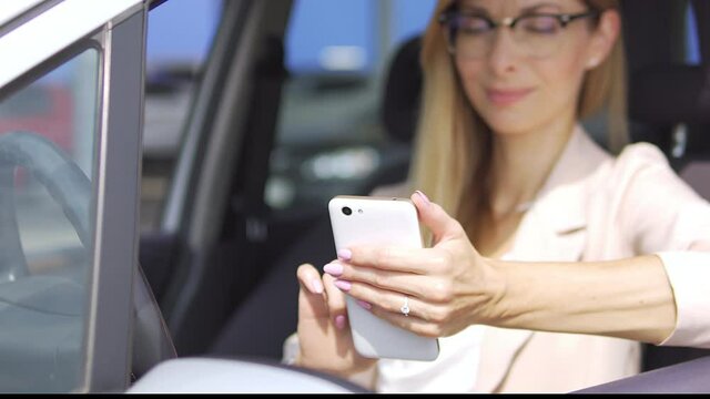 Beautiful elegant woman in business suit and stylish eyeglasses holding smartphone on hand and scrolling web-pages, future wife with big diamond engagement ring on fingers choosing dress online